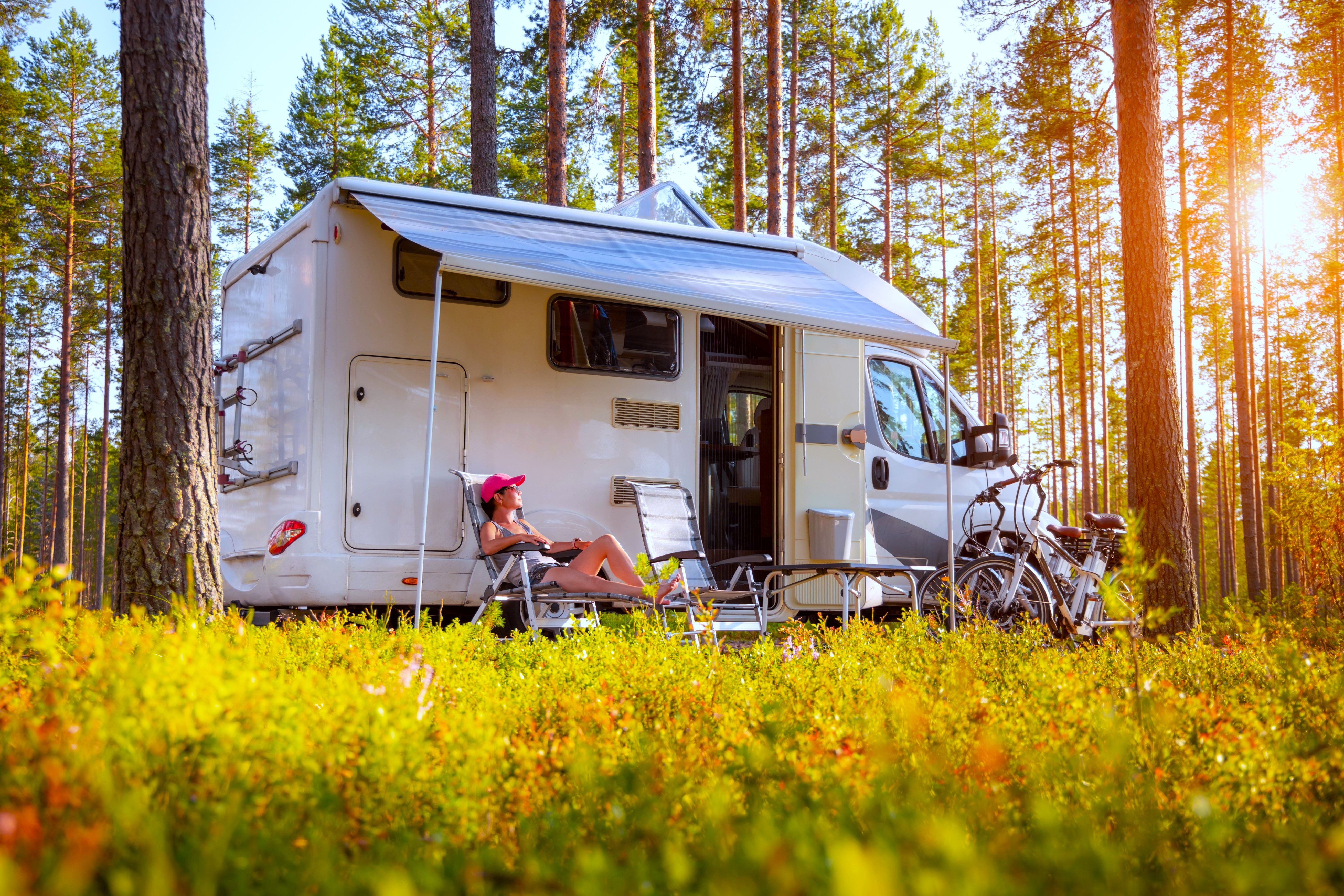 A woman sitting on a camping chair outside a camper van motorhome RV vehicle in a forest