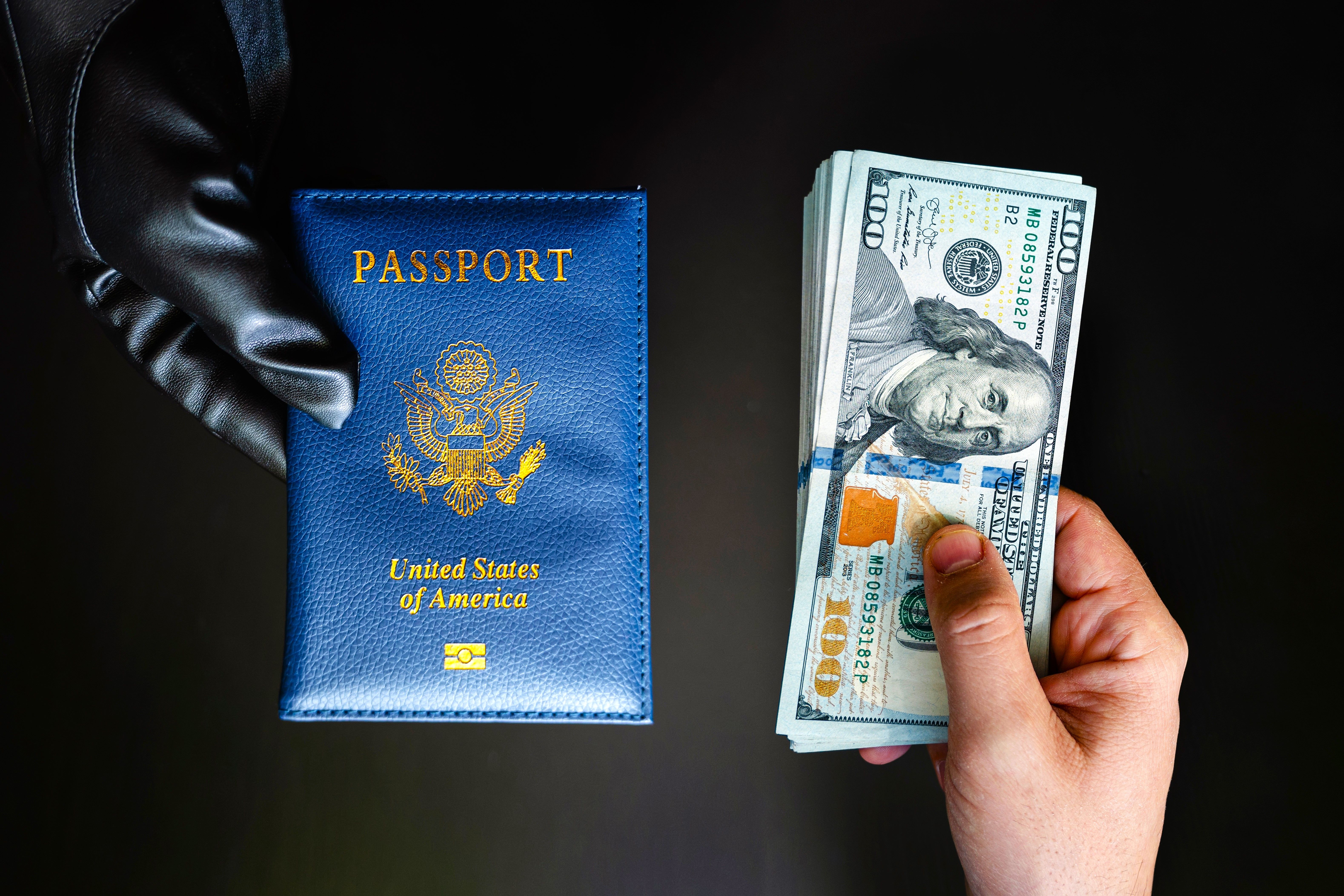 A person handing US dollar bills over to another person wearing gloves providing an American passport