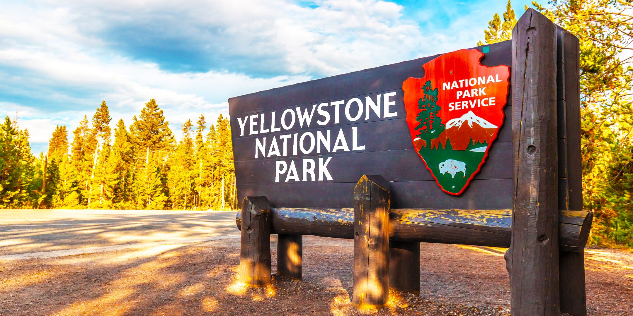 Entrance sign to Yellowstone National Park in front of a background of trees and cloudy sky