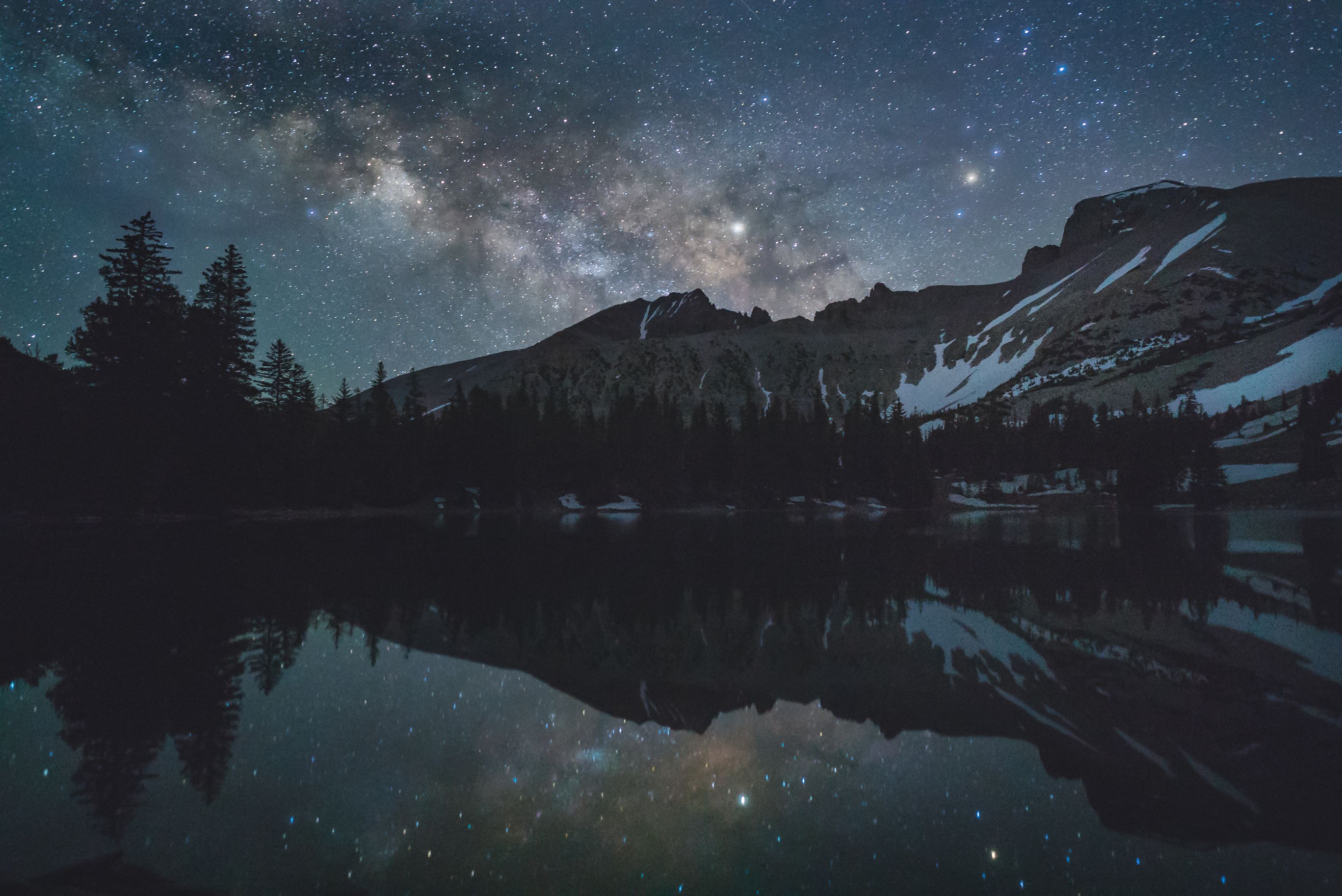 A view of a dark sky location at night at 11,000 feet in Great Basin National Park with the Milky Way over snowy mountains, reflected in a lake, Nevada, NV, USA.