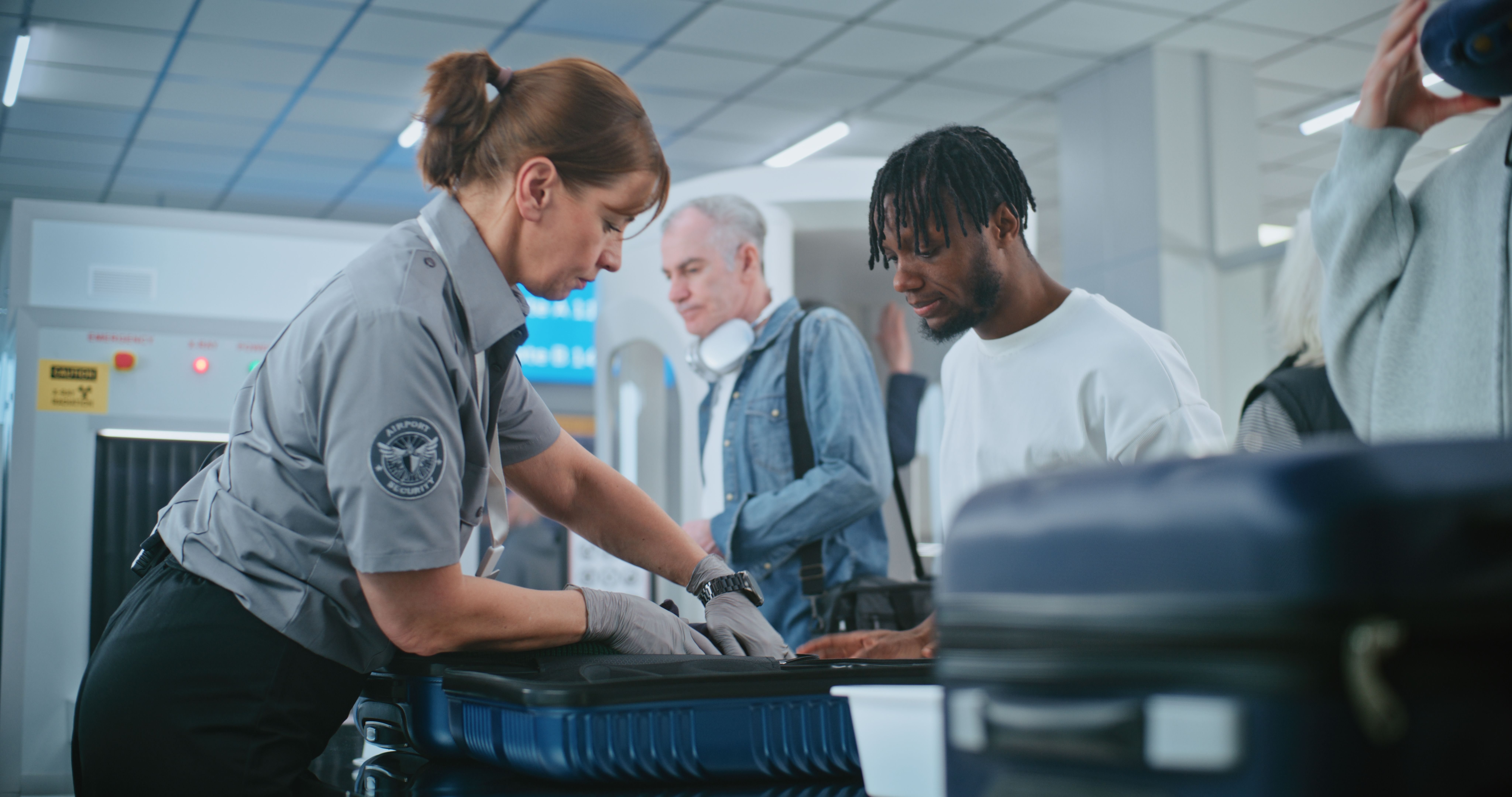 Security Checkpoint in Airport Terminal. Female TSA Worker Inspecting Baggage of Passenger