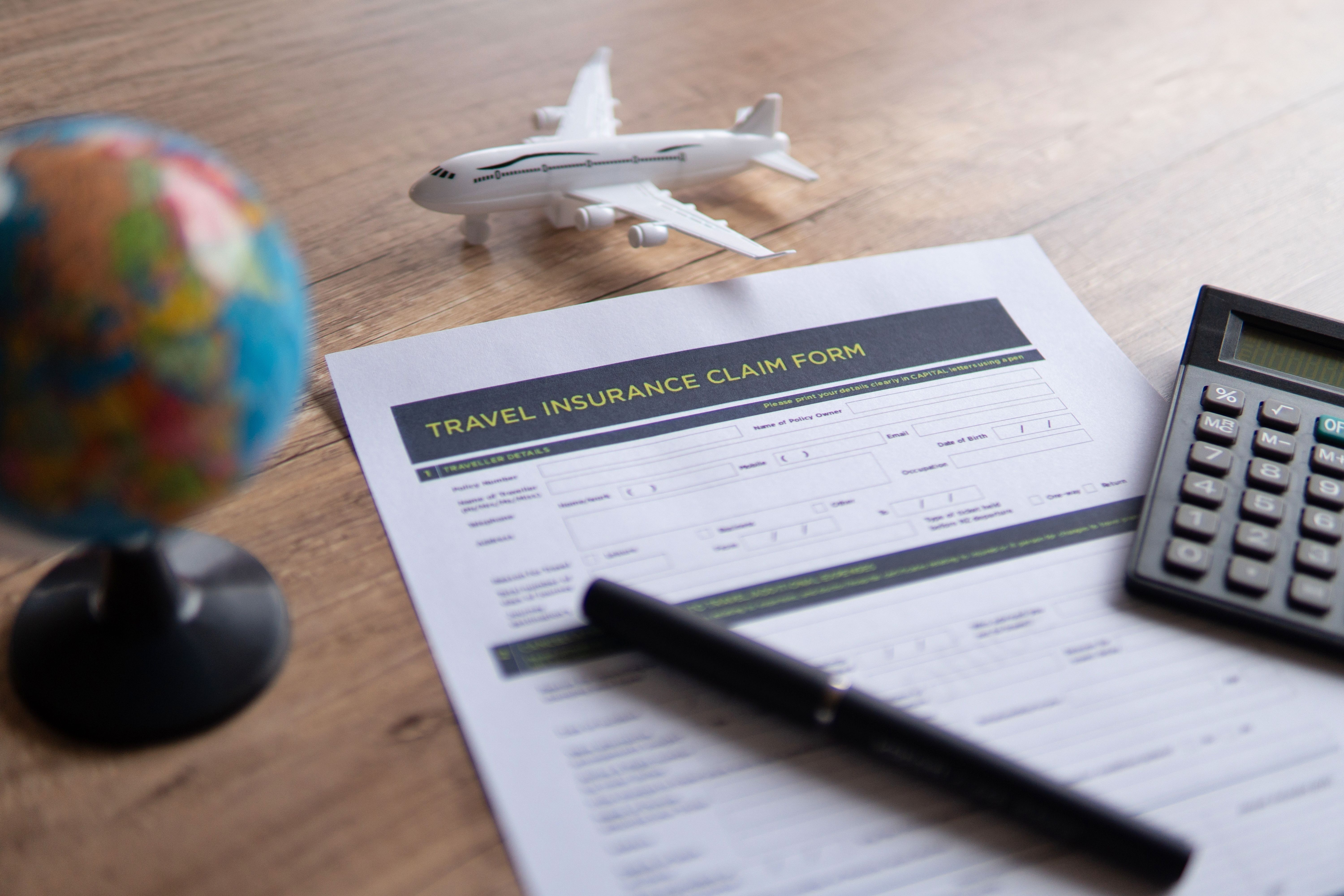 A travel insurance claim form on a wooden table, surrounded by a small globe, a toy airplane, a calculator and a pen.