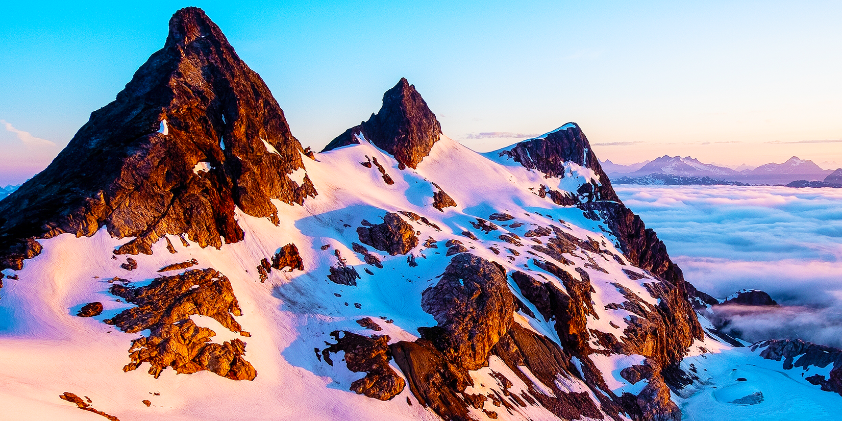 Rocky black mountain covered in white snow and glaciers during a pink sunset