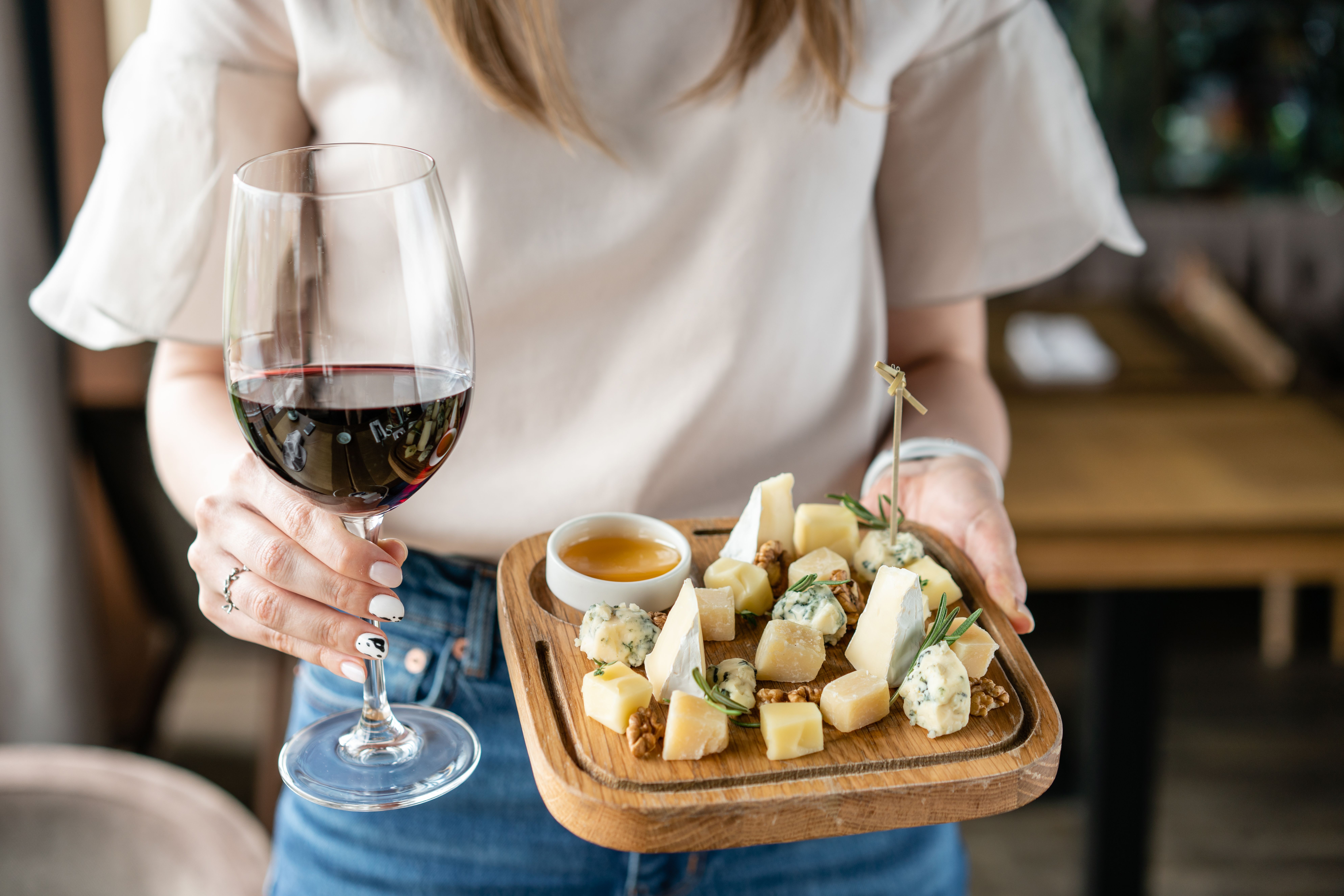 A woman holding an assorted cheese platter along with a glass of red wine.