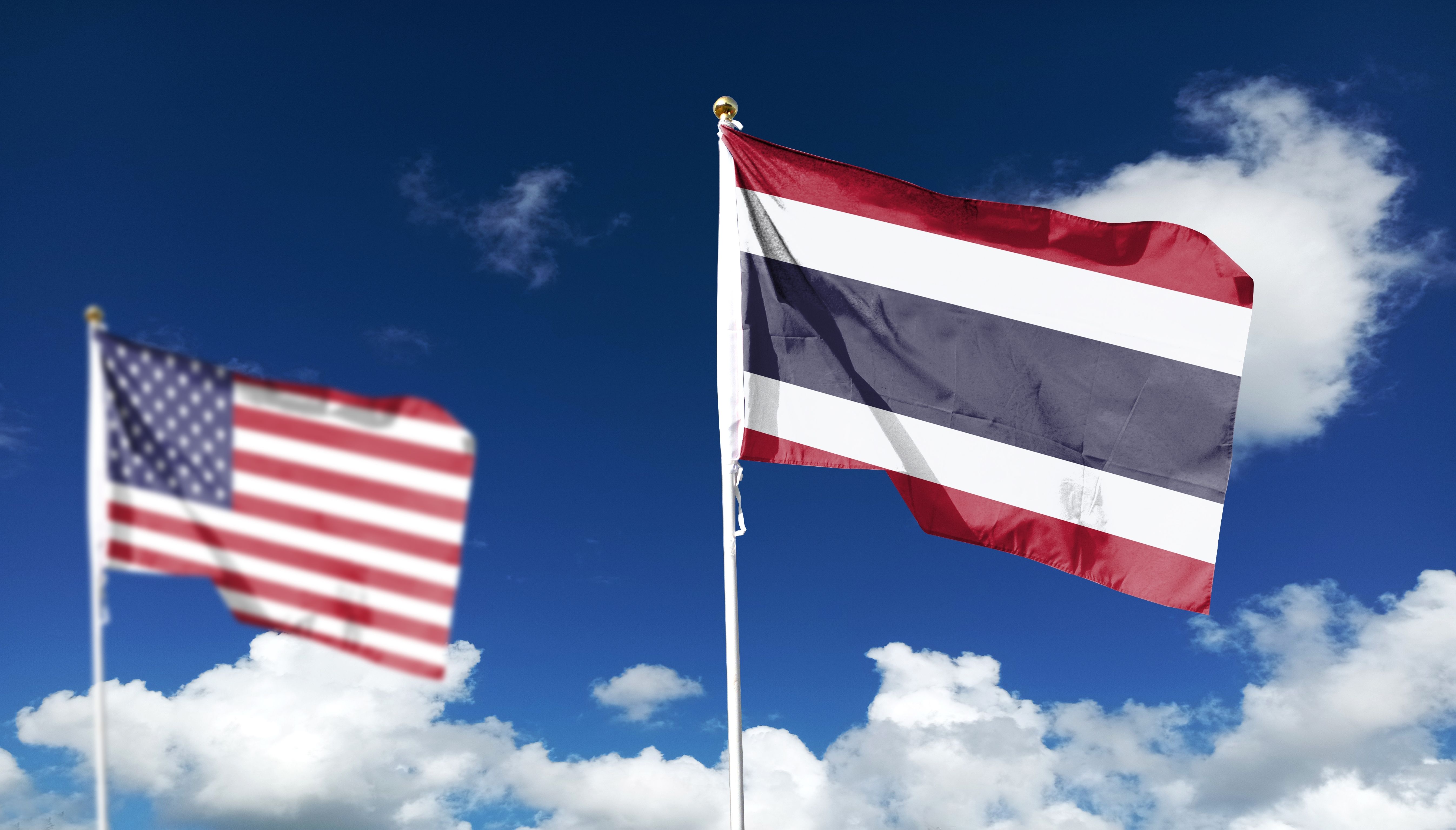 Thailand flag in the clear sky, with the American flag in the distance